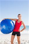 Fit blonde woman holding exercise ball on the beach