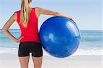 Fit blonde holding exercise ball looking at sea on the beach