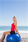 Smiling woman sitting on exercise ball looking at camera on the beach