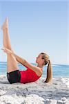 Athletic blonde doing pilates core exercise on the beach