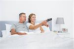 Happy couple watching tv in bed at home in bedroom