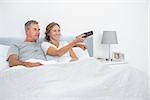 Cheerful couple watching tv in bed at home in bedroom