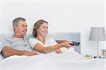 Smiling couple watching tv in bed at home in bedroom