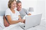 Smiling couple using their laptop together in bed at home in bedroom