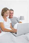 Cheerful couple using their laptop together in bed at home in bedroom
