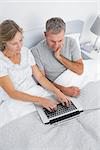 Thoughtful couple using their laptop together in bed at home in bedroom