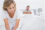 Couple sitting on opposite ends of bed after a fight at home in bedroom