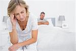 Upset couple sitting on opposite ends of bed after a fight in bedroom at home