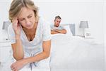 Unhappy couple sitting on opposite ends of bed after a fight in bedroom at home