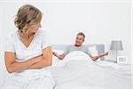 Angry woman looking at husband gesturing during a fight in bedroom at home