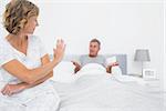 Annoyed woman looking at husband gesturing during a fight in bedroom at home