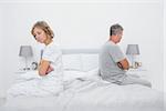Couple sitting on different sides of bed not talking after fight in bedroom at home