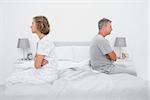 Couple sitting on different sides of bed not talking after dispute in bedroom at home