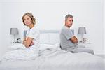 Couple sitting on different sides of bed not talking after argument looking at camera in bedroom at home