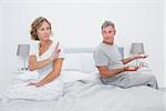 Couple sitting on different sides of bed having an argument in bedroom at home