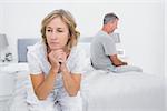 Unhappy couple sitting on different sides of bed having a dispute in bedroom at home