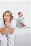 Fed up couple sitting on different sides of bed having a dispute with woman looking at camera in bedroom at home