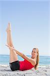 Athletic blonde doing pilates core exercise smiling at camera on the beach