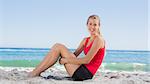 Athletic blonde sitting and smiling at camera on the beach