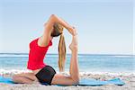 Fit blonde stretching leg in yoga pose on the beach