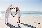 Loving couple forming heart shape with arms at the beach