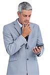 Thoughtful businessman against white background touching his chin and looking at his phone