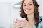 Cheerful brunette holding cup of coffee and looking at camera