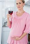 Expecting woman in her kitchen  holding glass of red wine