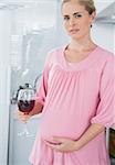 Expecting woman in her kitchen having glass of red wine