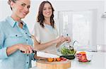 Woman cutting carrots with her friend mixing salad in the kitchen