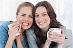 Smiling women holding their cup of coffee sitting on the sofa