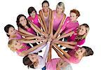 Cheerful women joined in a circle and looking up at camera wearing pink for breast cancer on white background