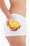 Toned female body holding half orange on white background