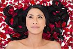 Pensive sensual dark haired model lying in rose petals on white background