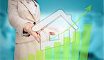 Businesswoman touching futuristic house interface with green bar chart on blurry office background