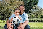 Smiling dad and son with a football in the park on sunny day