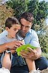 Dad and son inspecting leaf with a magnifying glass in the park