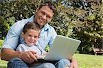 Smiling son and dad with a laptop on their knees in the park