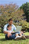 Cheerful dad and son with a laptop in a park