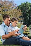 Dad and son playing with a tablet PC in a park together on sunny day