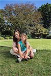 Cheerful mother and daughter on the grass in the park smiling at camera