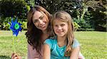 Happy mother and daughter holding pinwheel smiling at camera in the park