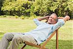 Happy mature man sitting on sun lounger and relaxing in park