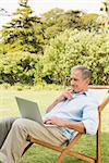 Happy mature man using laptop on sun lounger in park