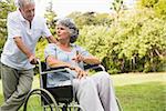 Mature woman in wheelchair speaking with partner in the park on sunny day