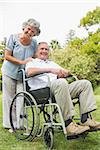 Cheeful mature man in wheelchair with partner smiling at camera in the park