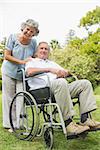 Smiling mature man in wheelchair with partner looking at camera in park