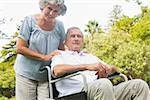 Cheerful mature man in wheelchair with his partner in park