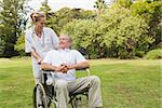 Smiling man sitting in a wheelchair talking with his nurse pushing him at the park