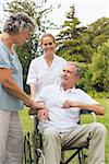 Happy man in a wheelchair talking with his nurse and wife in the park on sunny day